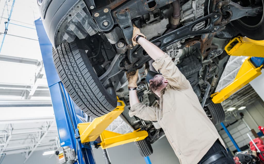 professional car mechanic performing lifted vehicle